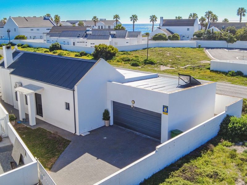 Aerial view of a modern white house with a corrugated metal roof, paved driveway, and integrated garage, situated in a coastal residential estate.