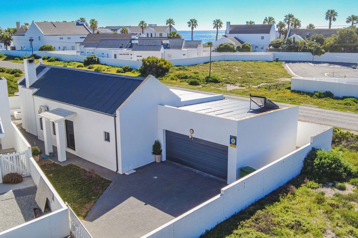 Aerial view of a modern white house with a corrugated metal roof, paved driveway, and integrated garage, situated in a coastal residential estate.