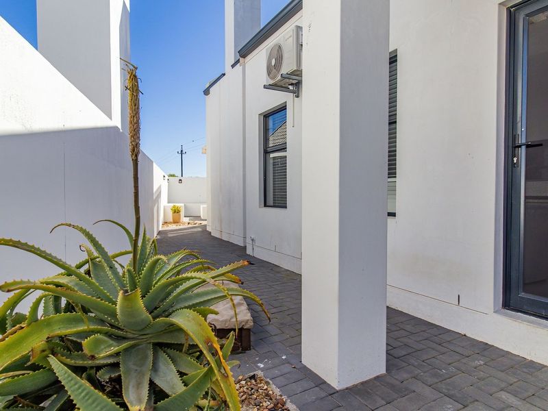 A clean, paved rear patio area featuring modern white exterior walls, aluminium framed windows and doors, and a wall-mounted air conditioning unit.