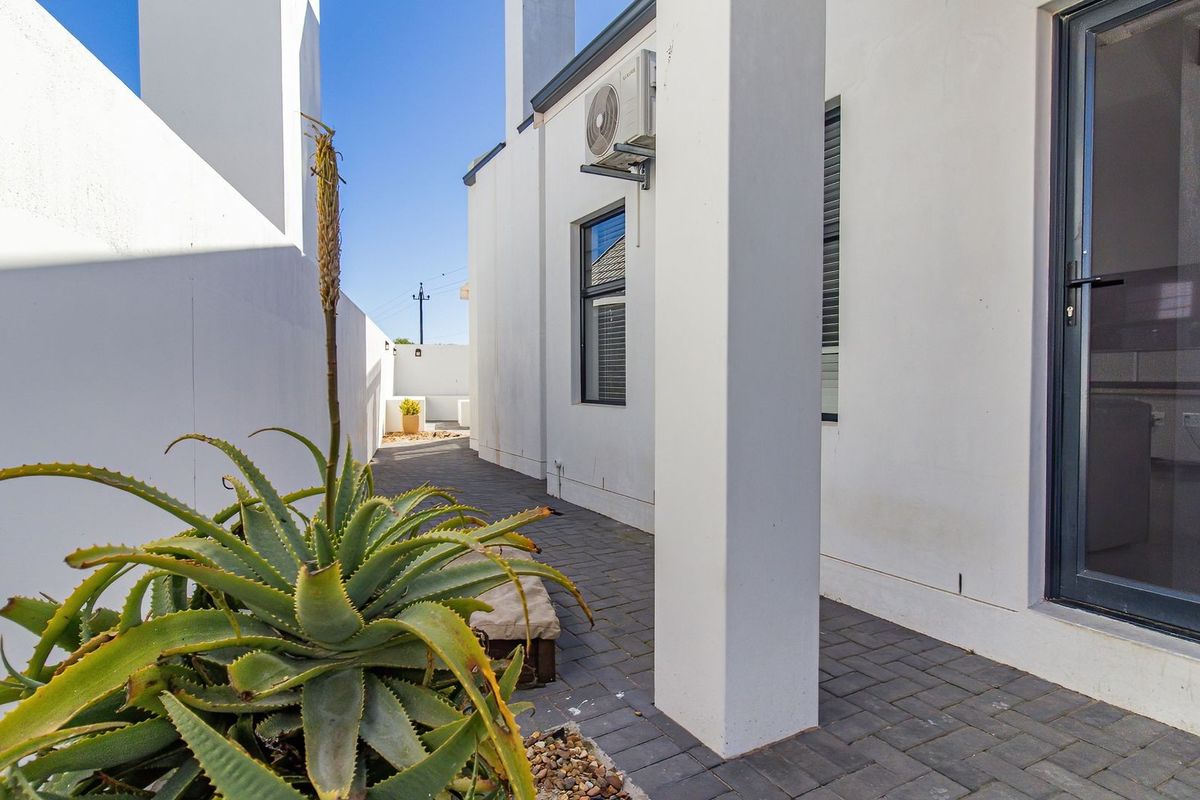 A clean, paved rear patio area featuring modern white exterior walls, aluminium framed windows and doors, and a wall-mounted air conditioning unit.