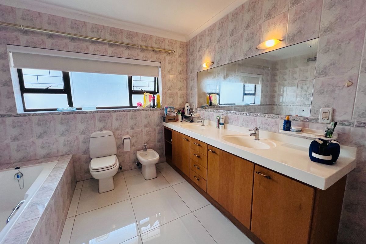 Spacious bathroom featuring a double vanity with wooden cabinetry, dual sinks, a built-in bathtub, toilet, and bidet, finished with patterned wall tiles.