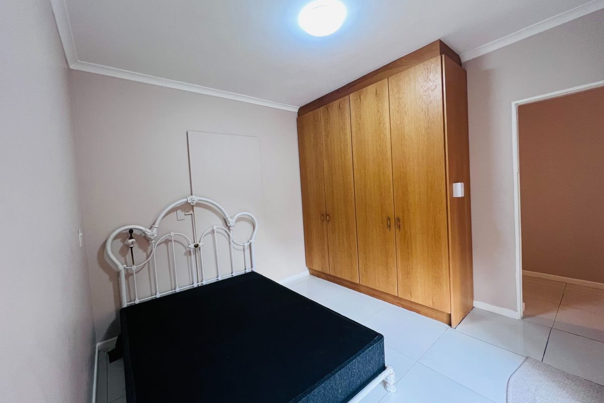 A bedroom featuring tiled flooring, neutral walls, and a large built-in wooden wardrobe providing ample storage space.