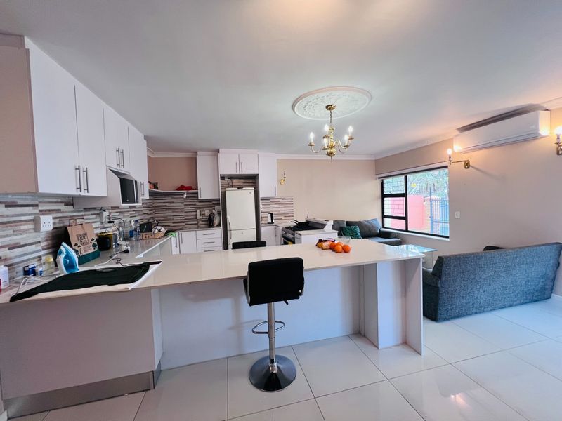 Open-plan living area featuring a modern kitchen with white cabinetry, stone countertops, breakfast bar, and tiled flooring, seamlessly flowing into the lounge space.
