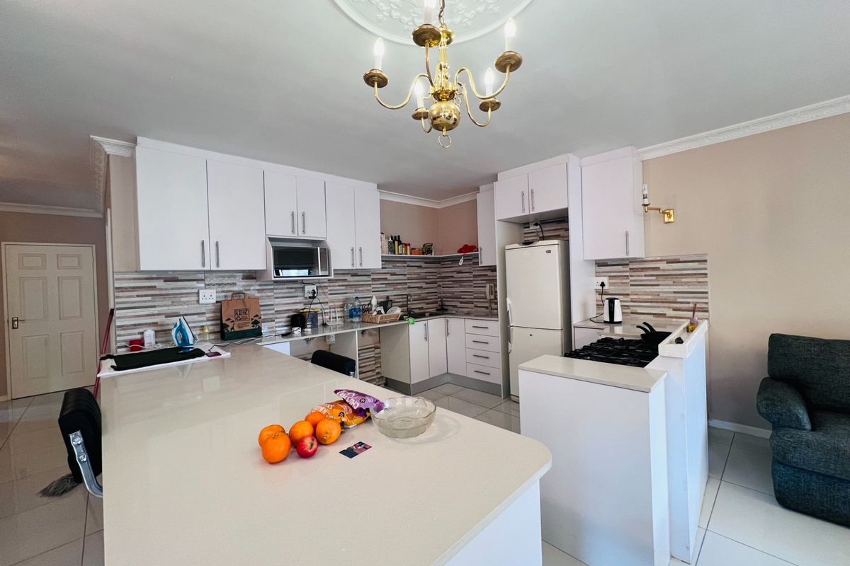 A functional kitchen featuring white cabinetry, stone countertops, a gas hob, and a tiled backsplash, complemented by a decorative ceiling rose and chandelier.