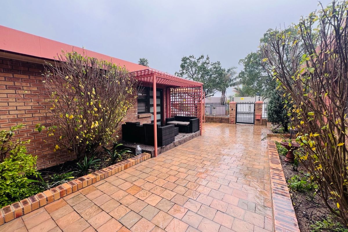 A paved rear courtyard area featuring a built-in pergola structure, brick exterior walls, and secure perimeter fencing with a metal gate.