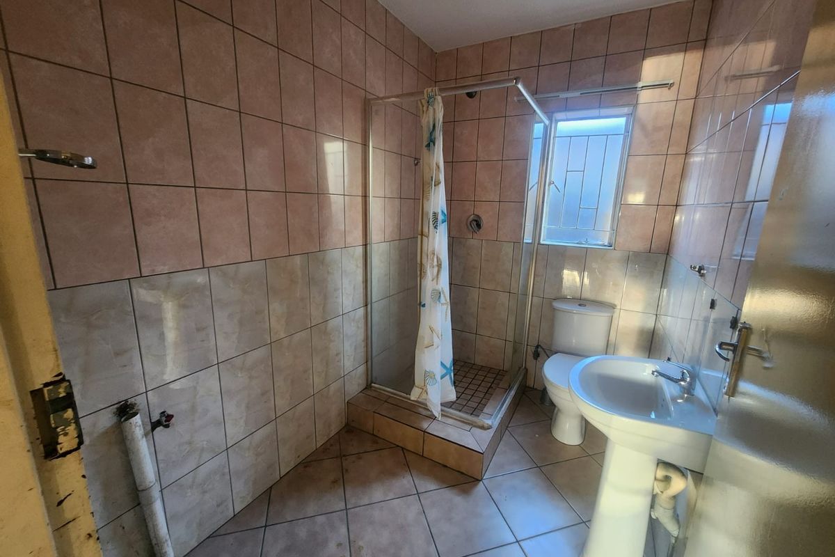 A dated bathroom featuring a shower enclosure, pedestal basin, and toilet, with tiled walls and flooring. The space requires cosmetic updates and minor repairs.