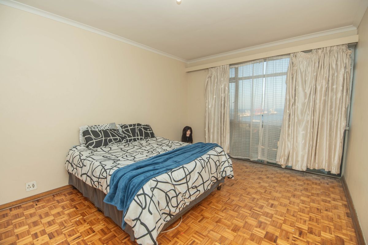 A bedroom featuring classic parquet flooring and a large sliding glass door that provides natural light and access to the balcony.