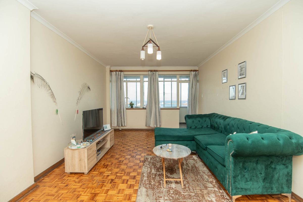 A living room featuring classic parquet flooring, coved ceilings, and large windows that provide natural light and a view of the ocean.