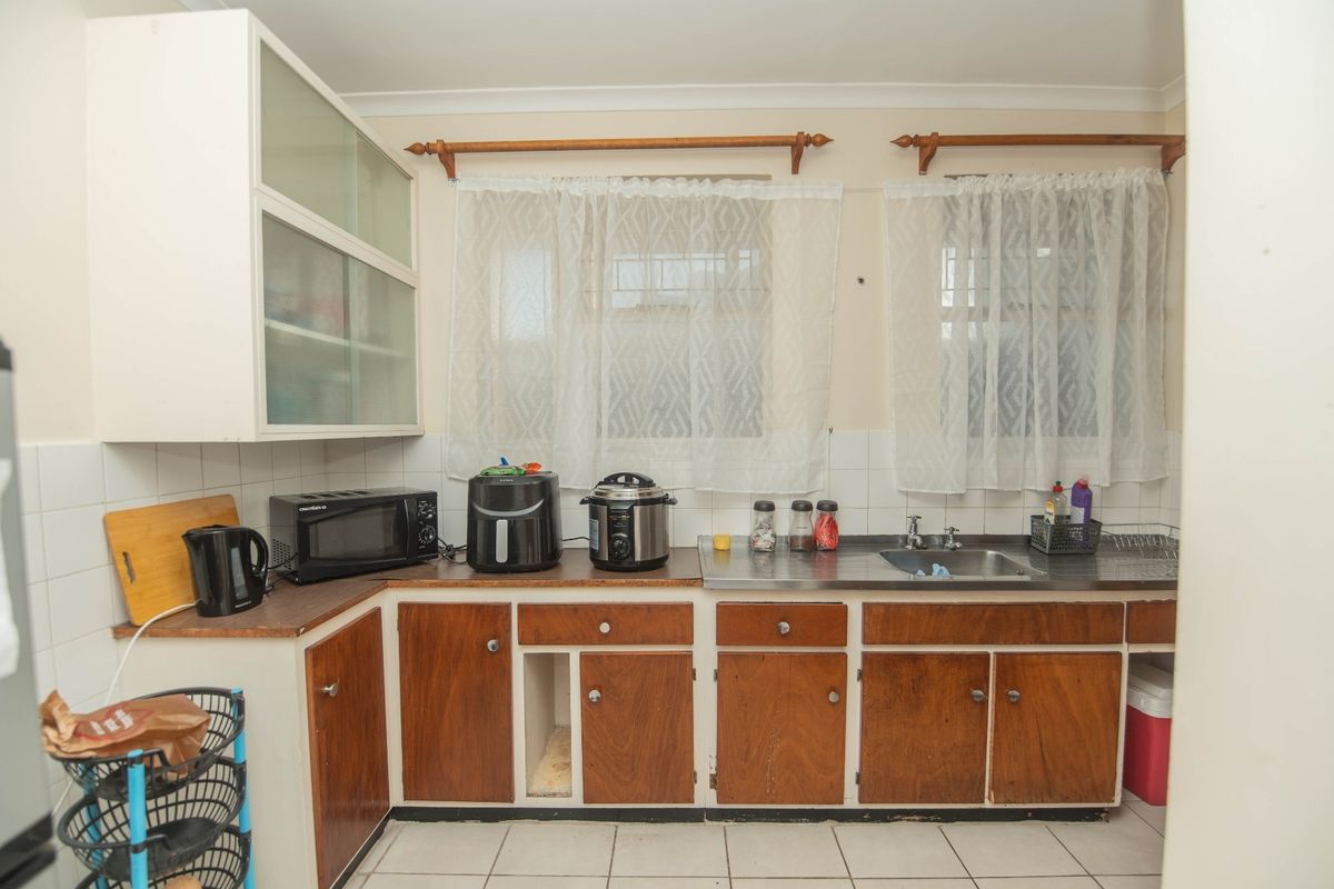 A dated kitchen featuring wood-finish cabinetry, a stainless steel sink, tiled splashbacks, and ceramic floor tiles, offering potential for modernization.