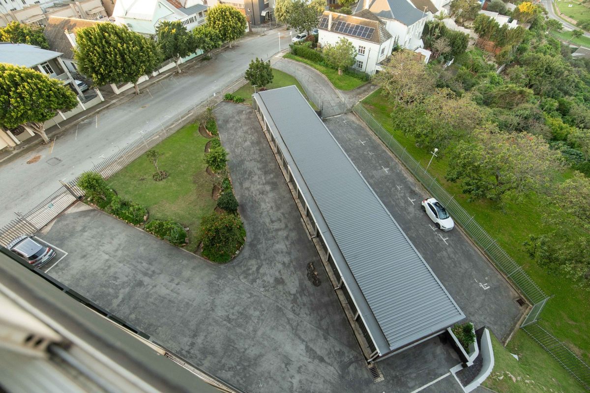 Aerial view of the apartment complex grounds, featuring a covered parking structure, paved driveway, and surrounding landscaped garden areas.