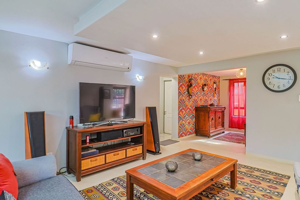 A well-maintained living room featuring recessed lighting, a wall-mounted air conditioning unit, and an open-plan layout leading to an adjacent space.