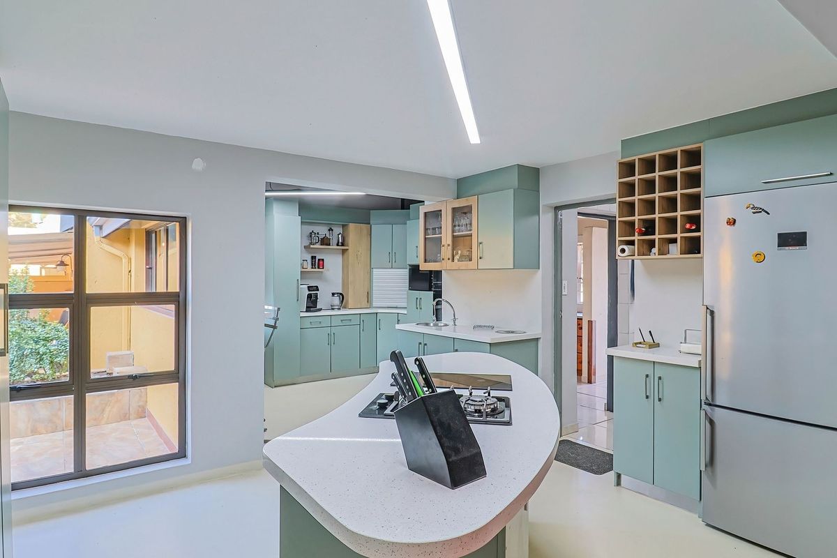 A functional kitchen featuring light green cabinetry, a central island with a gas hob, and a secondary prep area visible in the background.
