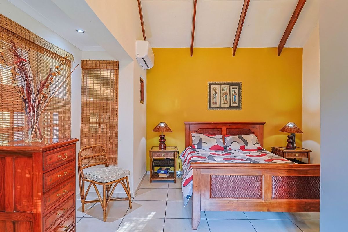 A bedroom featuring exposed timber ceiling beams, tiled flooring, and a wall-mounted split-system air conditioner.