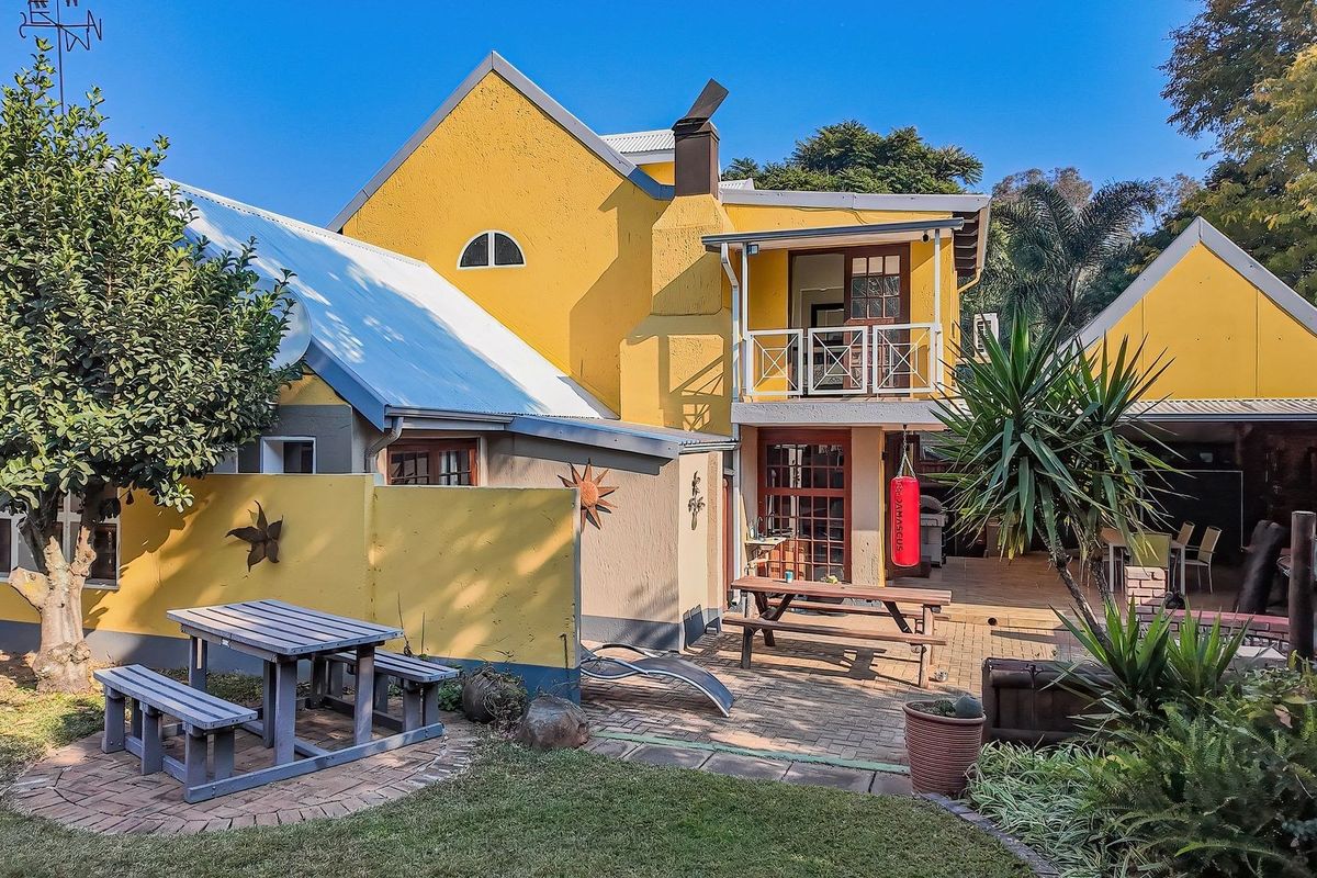 Rear view of the guest house featuring a paved patio area, upper-level balcony, and yellow exterior walls with mature garden landscaping.