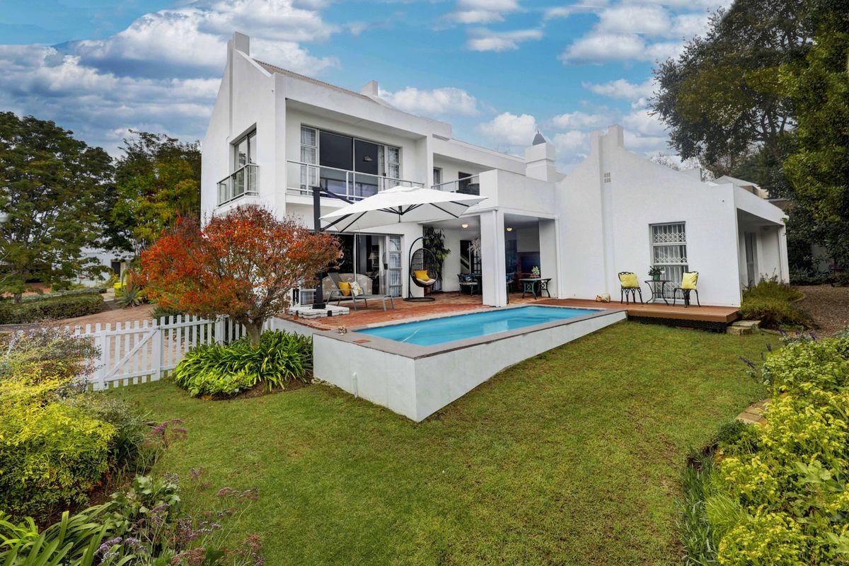 Rear view of the property featuring a swimming pool, covered patio area, timber decking, and a well-maintained garden with a white picket fence.