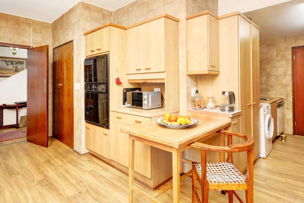A functional kitchen featuring light wood cabinetry, a double wall oven, tiled wall finishes, and integrated laundry space with wood-look flooring.