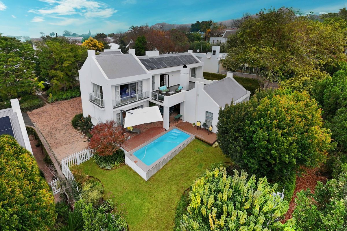 Aerial view of a well-maintained residential property featuring a swimming pool, solar panels, balcony, and landscaped garden area.