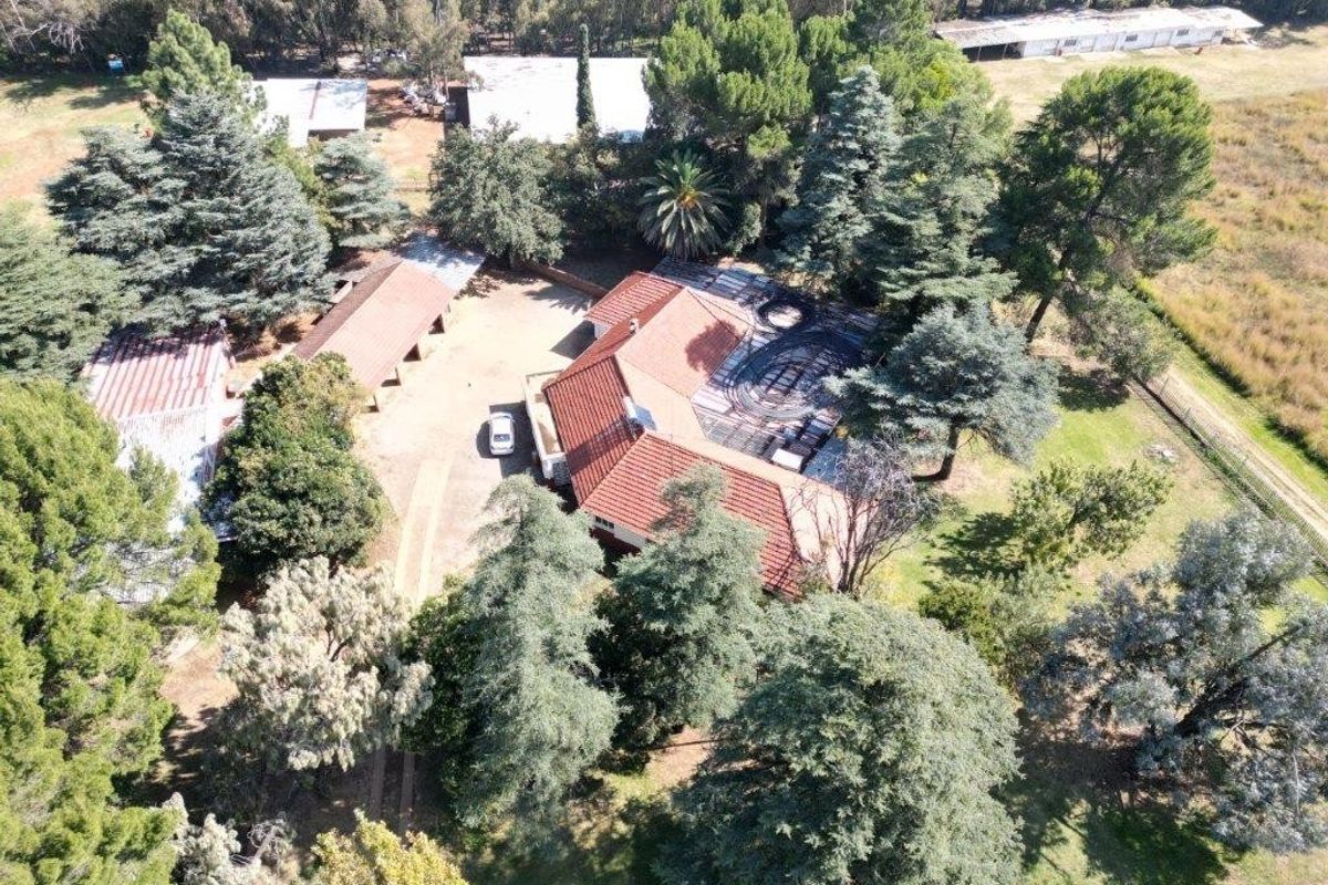Aerial view of a small holding property featuring a main residence with a tiled roof, multiple outbuildings, and extensive mature garden landscaping.