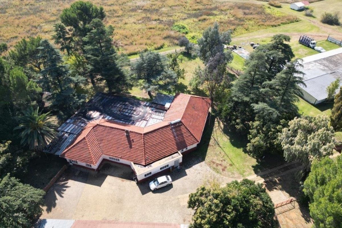Aerial view of a small holding property featuring a main residence with a tiled roof, surrounding mature trees, and extensive outdoor grounds.
