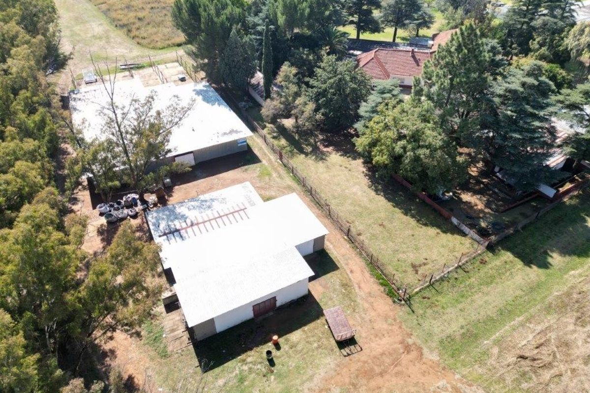 Aerial view of the small holding property featuring multiple outbuildings, established trees, and fenced grounds.