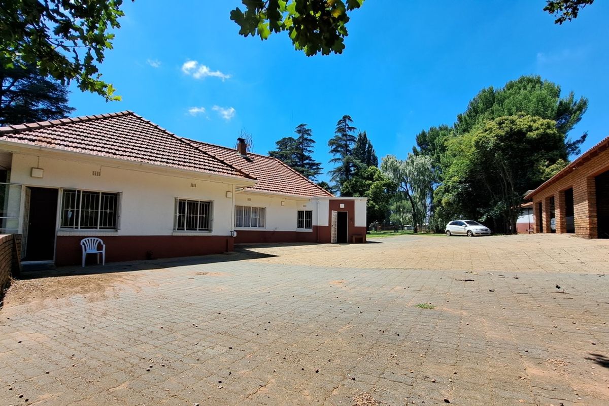 Rear view of the main dwelling featuring a tiled roof and brick paving, with an adjacent brick outbuilding on a spacious small holding property.