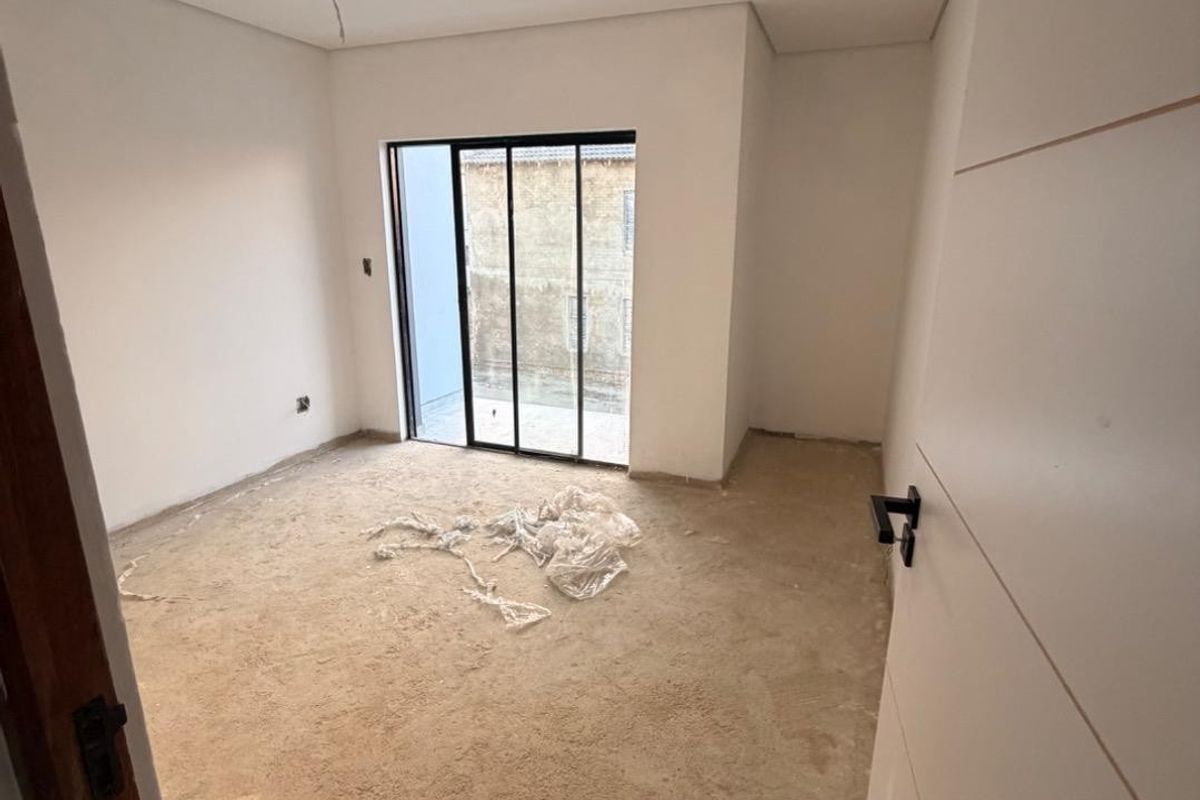 An unfinished bedroom space featuring white walls, a modern black-framed sliding glass door, and bare concrete flooring awaiting final finishes.