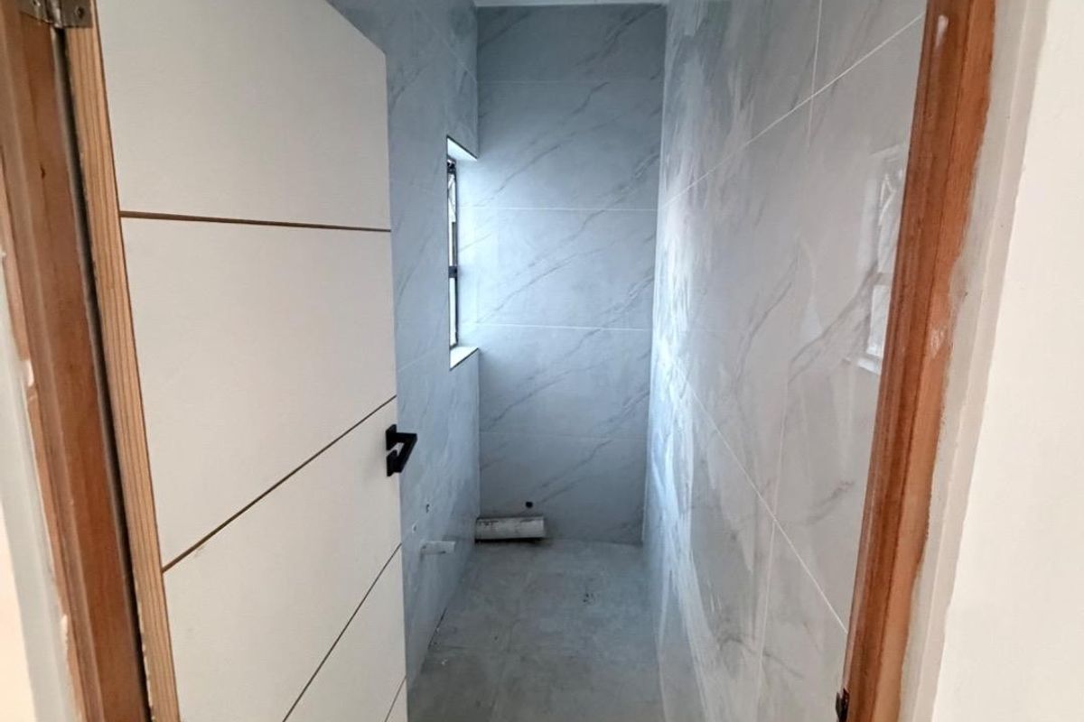 An unfinished bathroom space featuring marble-look wall tiles, plumbing rough-ins, and exposed electrical wiring, awaiting final fixtures and completion.