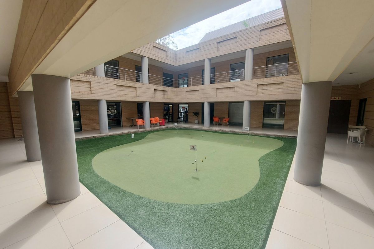 A central courtyard featuring a putting green, surrounded by a two-story office building with covered walkways and brick architecture.