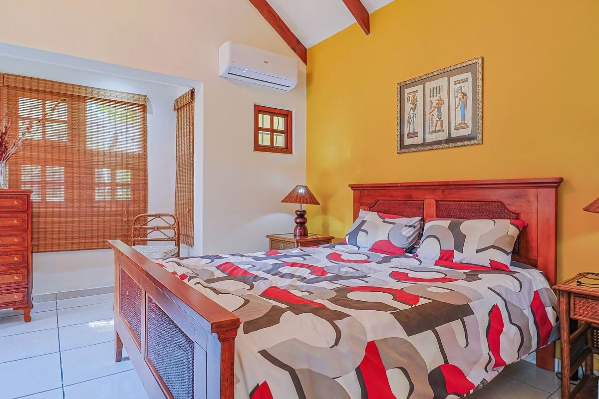 A bedroom featuring vaulted ceilings with exposed timber beams, tiled flooring, and a wall-mounted split-system air conditioner.