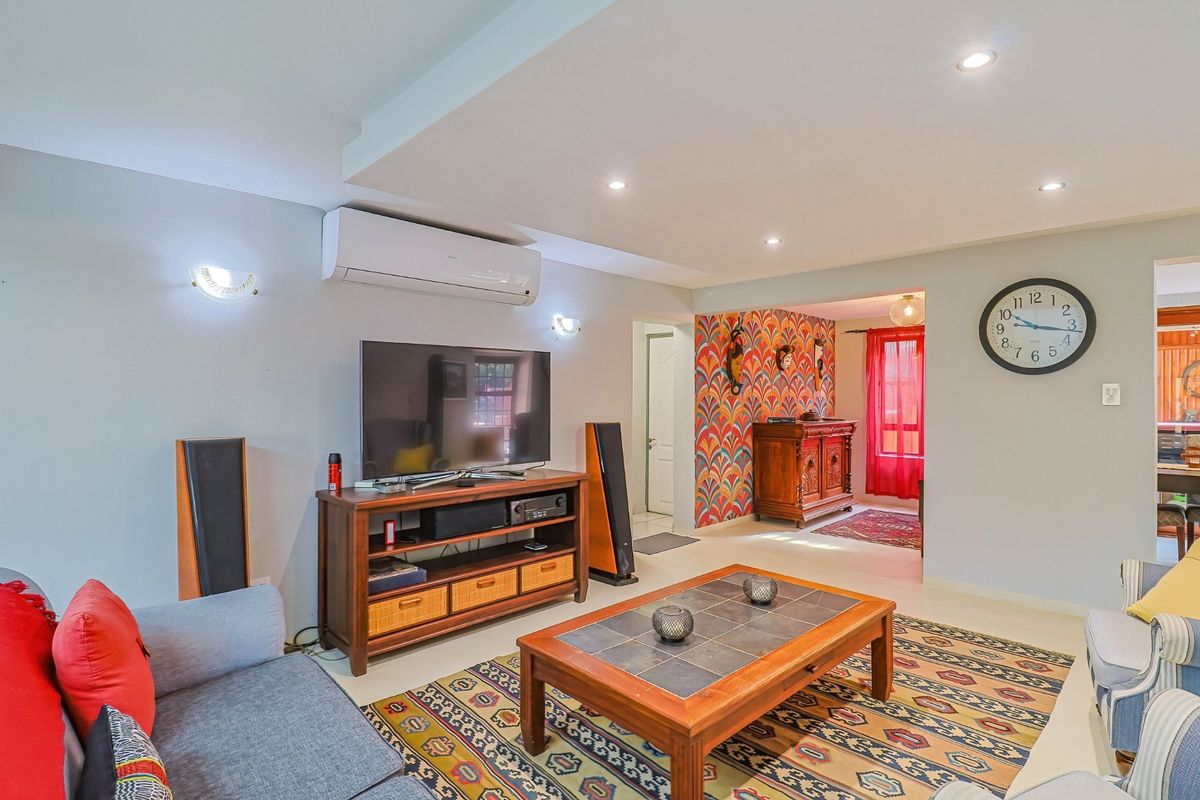 A comfortable living room featuring recessed downlighting, wall sconces, and a wall-mounted split-system air conditioner, leading into an adjacent dining area.