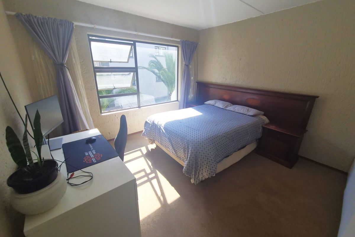 A bedroom featuring a built-in wooden headboard, carpeted flooring, and large aluminium-framed windows allowing natural light.