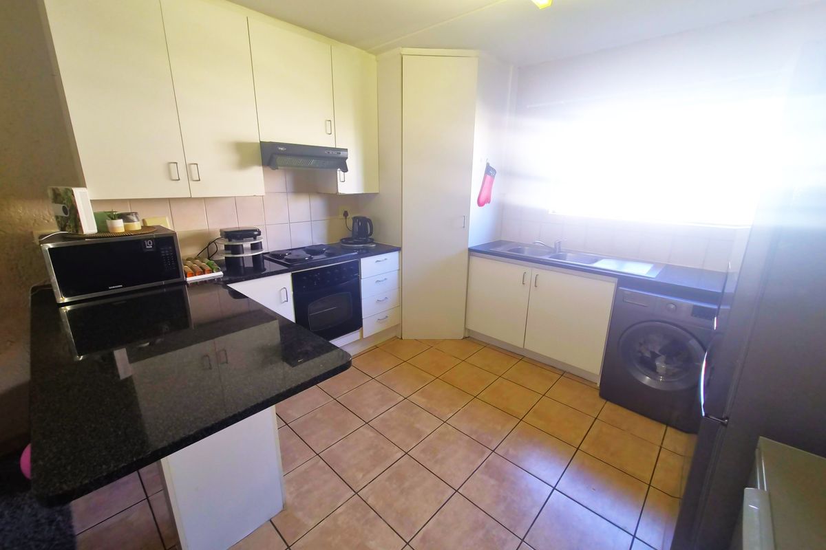 Functional kitchen featuring white cabinetry, dark granite countertops, tiled flooring, and integrated appliances including an oven, hob, and extractor fan.