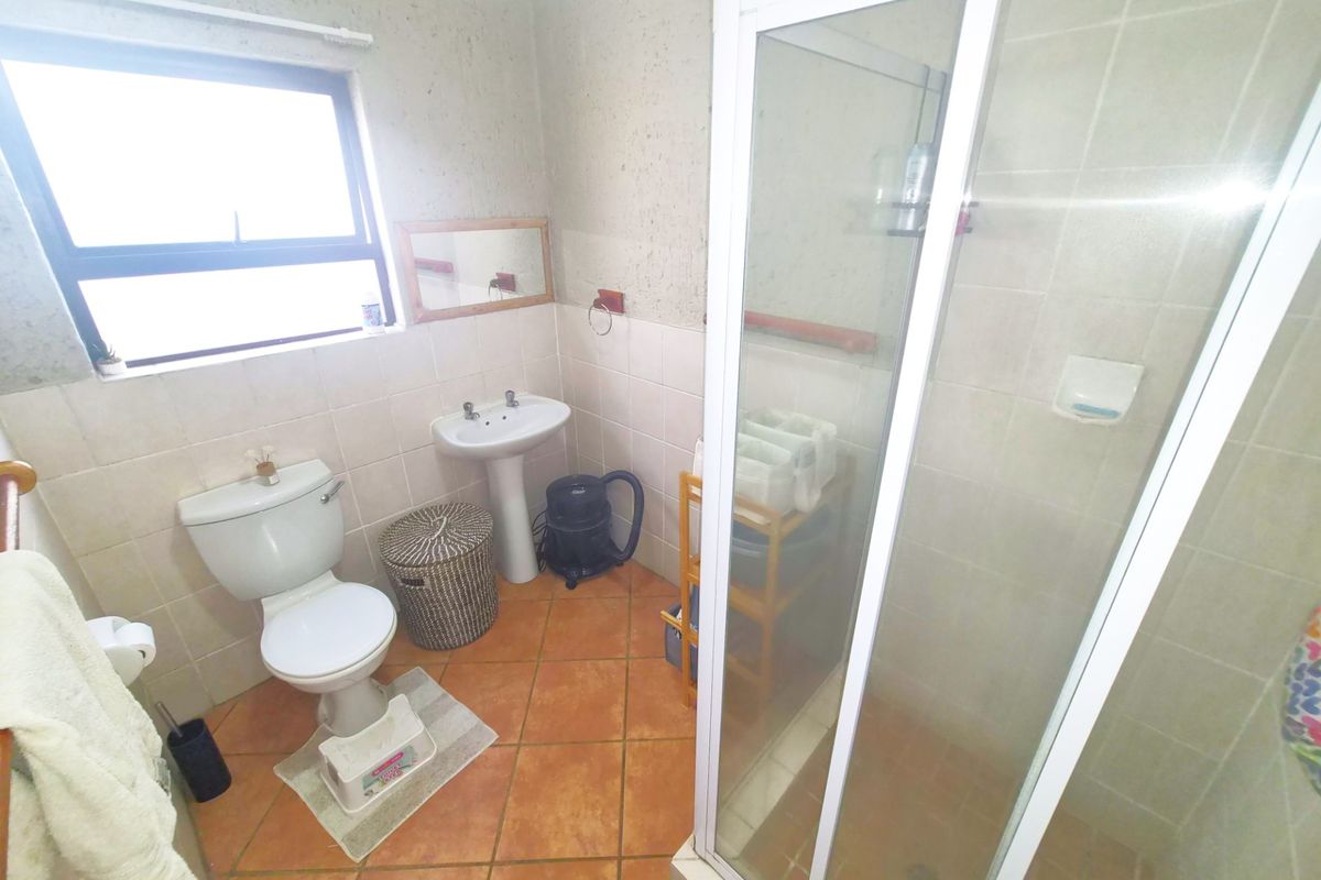 A functional bathroom featuring a pedestal basin, toilet, and a glass-enclosed shower with tiled walls and flooring.