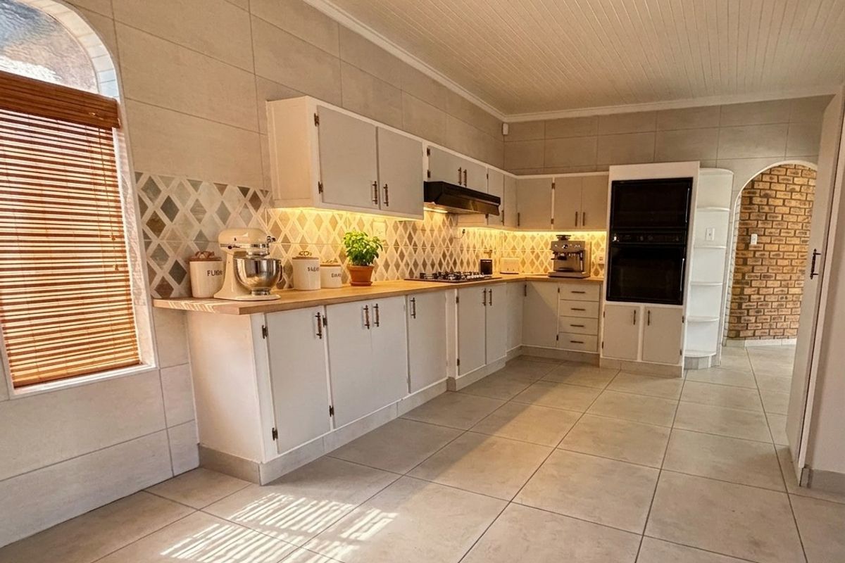 A well-maintained kitchen featuring light-toned cabinetry, timber countertops, a built-in oven, and a decorative tiled splashback with integrated under-cabinet lighting.