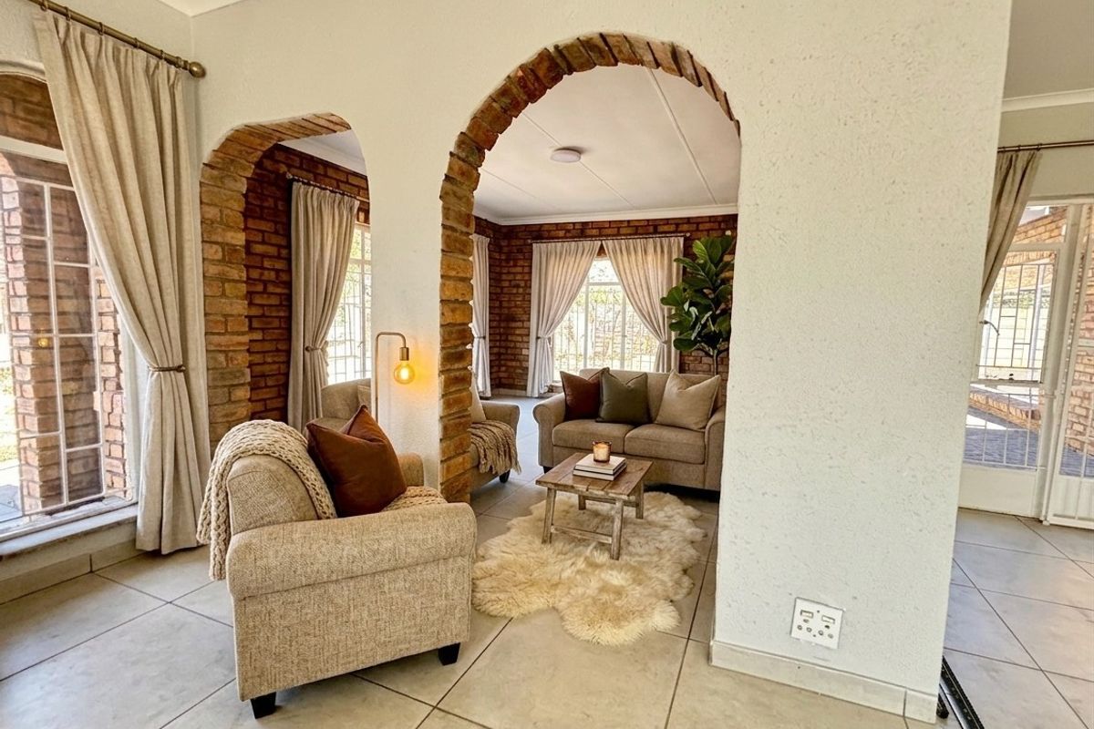 A cozy living area featuring distinctive exposed brick archways, neutral tiled flooring, and abundant natural light through large windows with security gates.