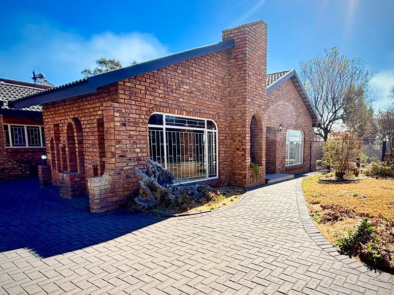 Front elevation of a face-brick house featuring arched architectural details, security bars on windows, and a paved driveway leading to the entrance.