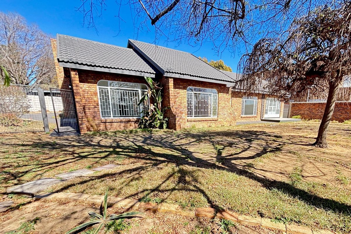 Rear view of a face brick house featuring a tiled roof, security bars on windows, and a spacious garden area.