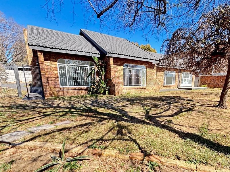 Rear view of a face brick house featuring a tiled roof, security bars on windows, and a spacious garden area.