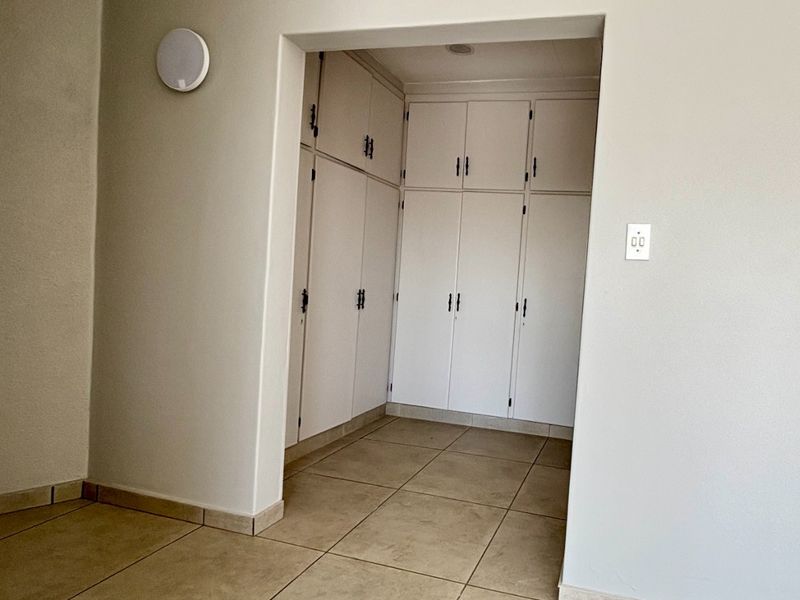 A clean, empty hallway featuring neutral tiled flooring and extensive built-in storage cabinetry with white doors.
