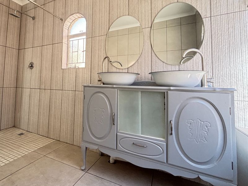 Modern bathroom featuring a double vanity with vessel sinks, a walk-in shower, and floor-to-ceiling tiled walls with an arched window.