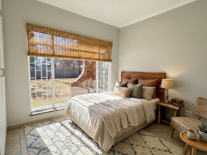 A bright and well-maintained bedroom featuring tiled flooring, a built-in cupboard, and a sliding glass door providing direct access to the rear garden.
