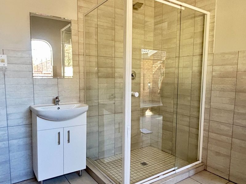 A clean, modern bathroom featuring a glass-enclosed shower, a white vanity basin, and neutral-toned wall and floor tiling.