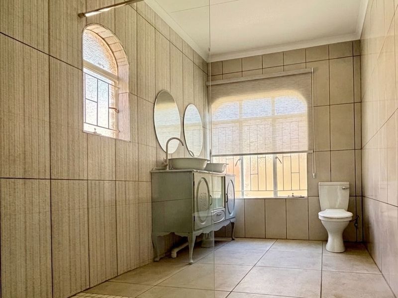A modern bathroom featuring a glass-enclosed shower, double vanity, and neutral floor-to-ceiling tiling with natural light from arched windows.