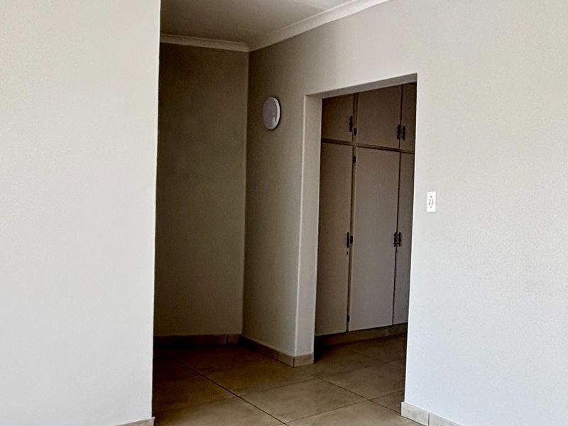 A clean, neutral hallway featuring tiled flooring and built-in storage cupboards, providing a functional transition space within the home.
