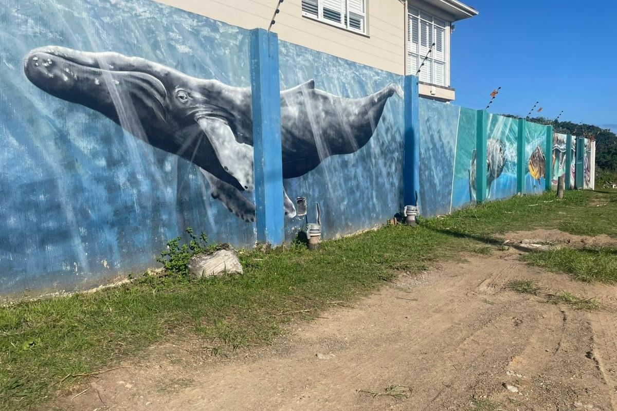 A view of a residential boundary wall featuring a large whale mural and integrated electric fencing.