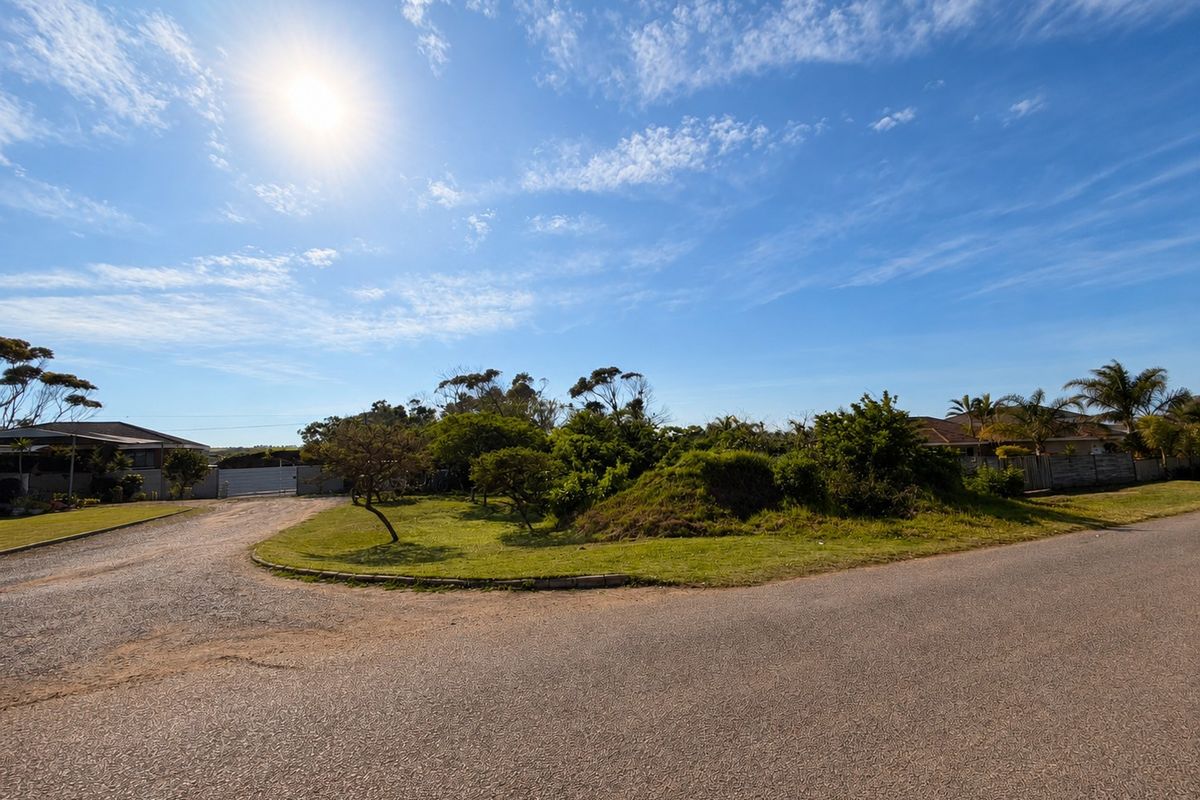 A street-level view of a vacant residential plot featuring established landscaping, grassed areas, and paved road access in a quiet neighborhood setting.