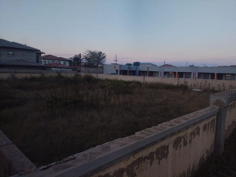 A vacant residential plot enclosed by a perimeter wall, featuring overgrown grass and clear boundaries in a suburban neighborhood setting.