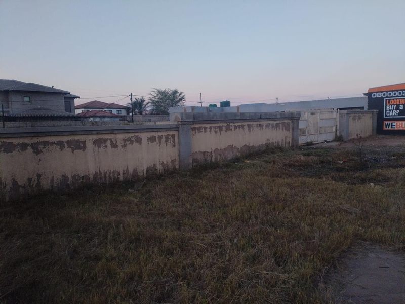 A view of the vacant residential plot featuring a perimeter wall and boundary gate, showing signs of exterior weathering.