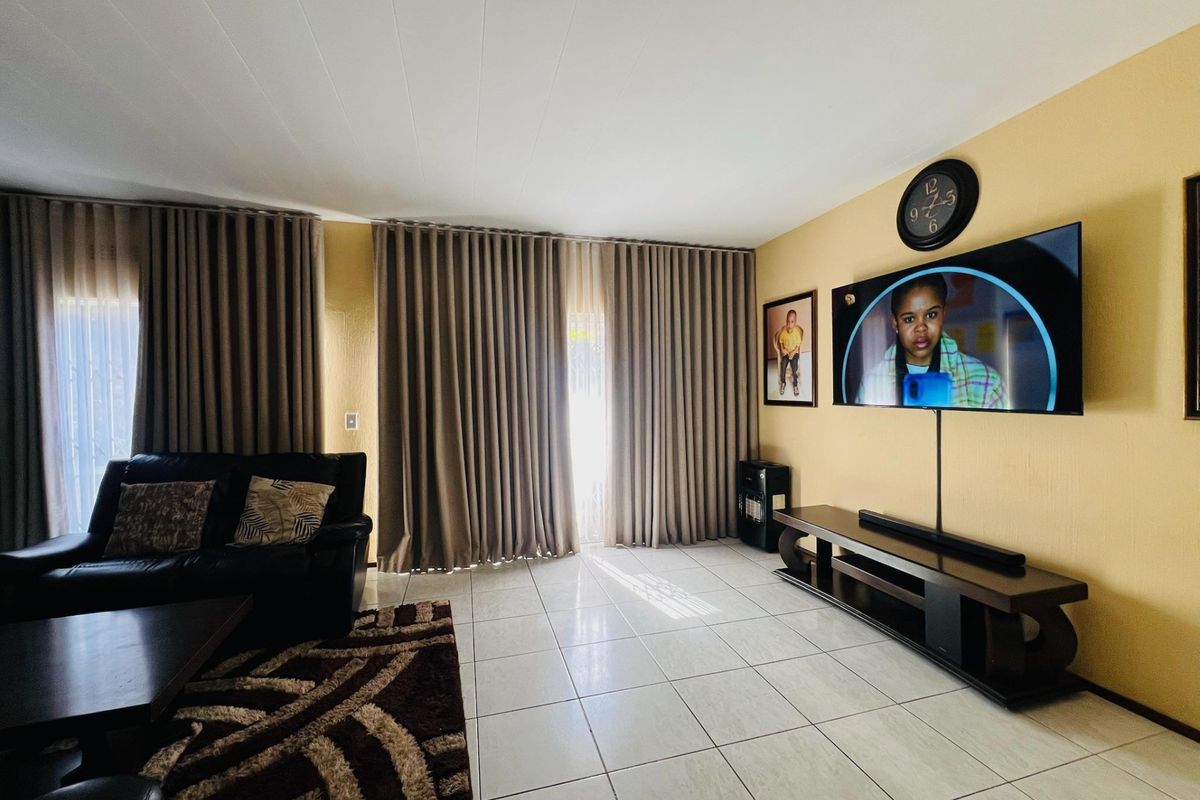 A well-maintained living room featuring neutral tiled flooring and floor-to-ceiling curtains providing access to the outdoor area.