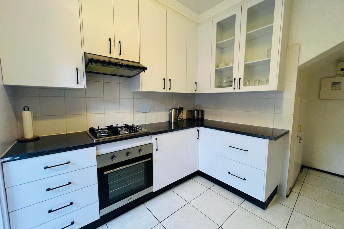A well-maintained kitchen featuring white cabinetry, black granite countertops, a gas hob, built-in oven, and tiled flooring.